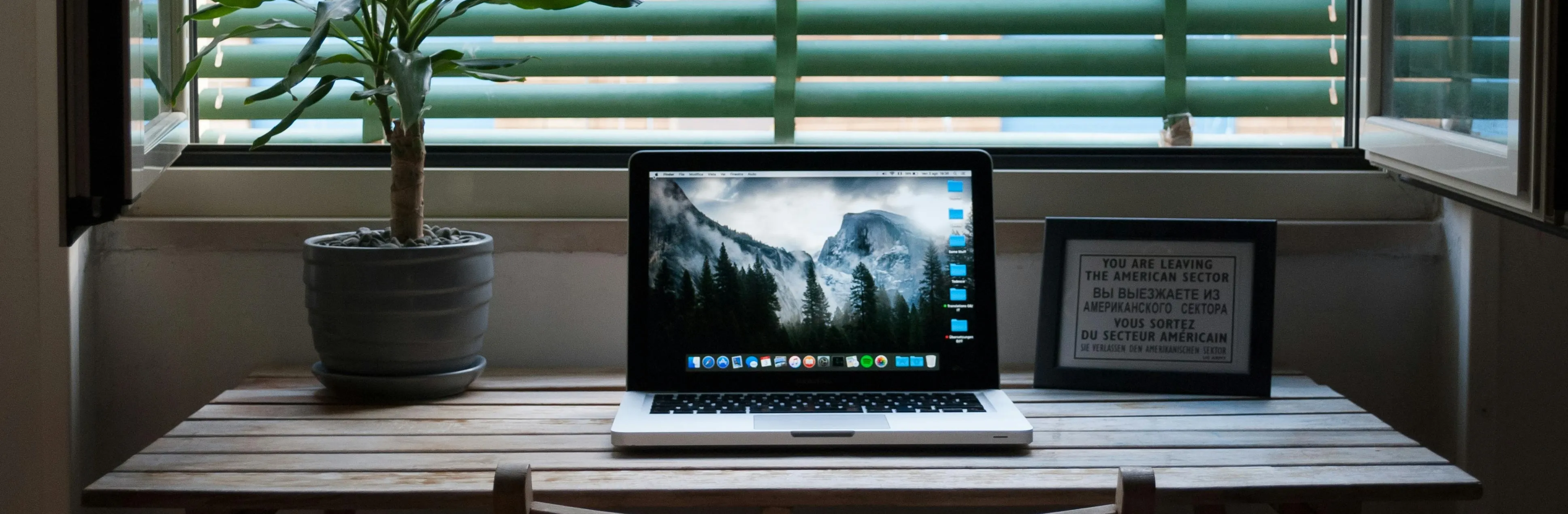 Minimalist workspace with a MacBook laptop showing a clean interface, ideal for UI/UX design, on a wooden desk next to an indoor plant and natural light coming in through the window.